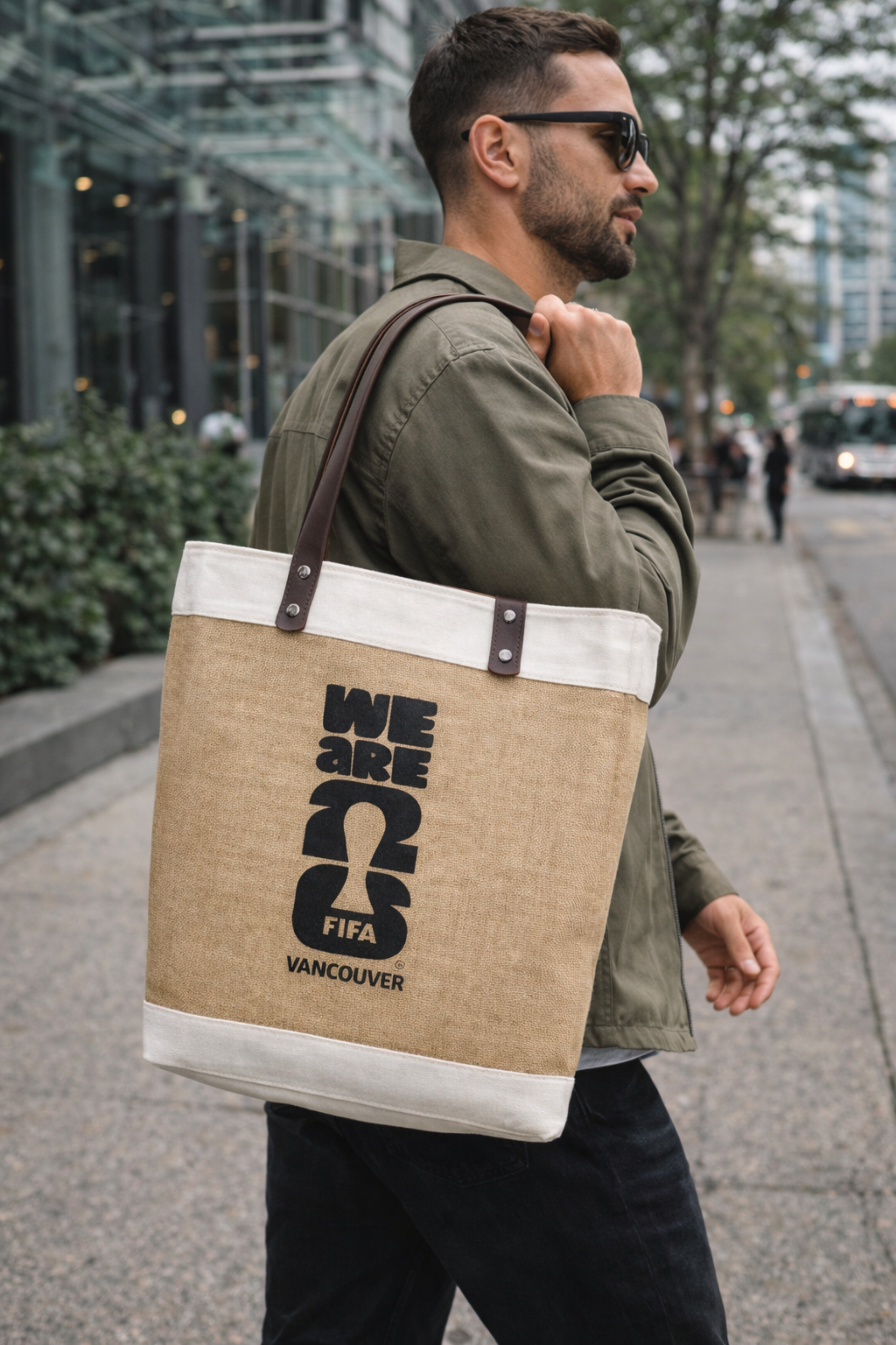 Man carrying a market tote bag with FIFA Vancouver branding on a city street.